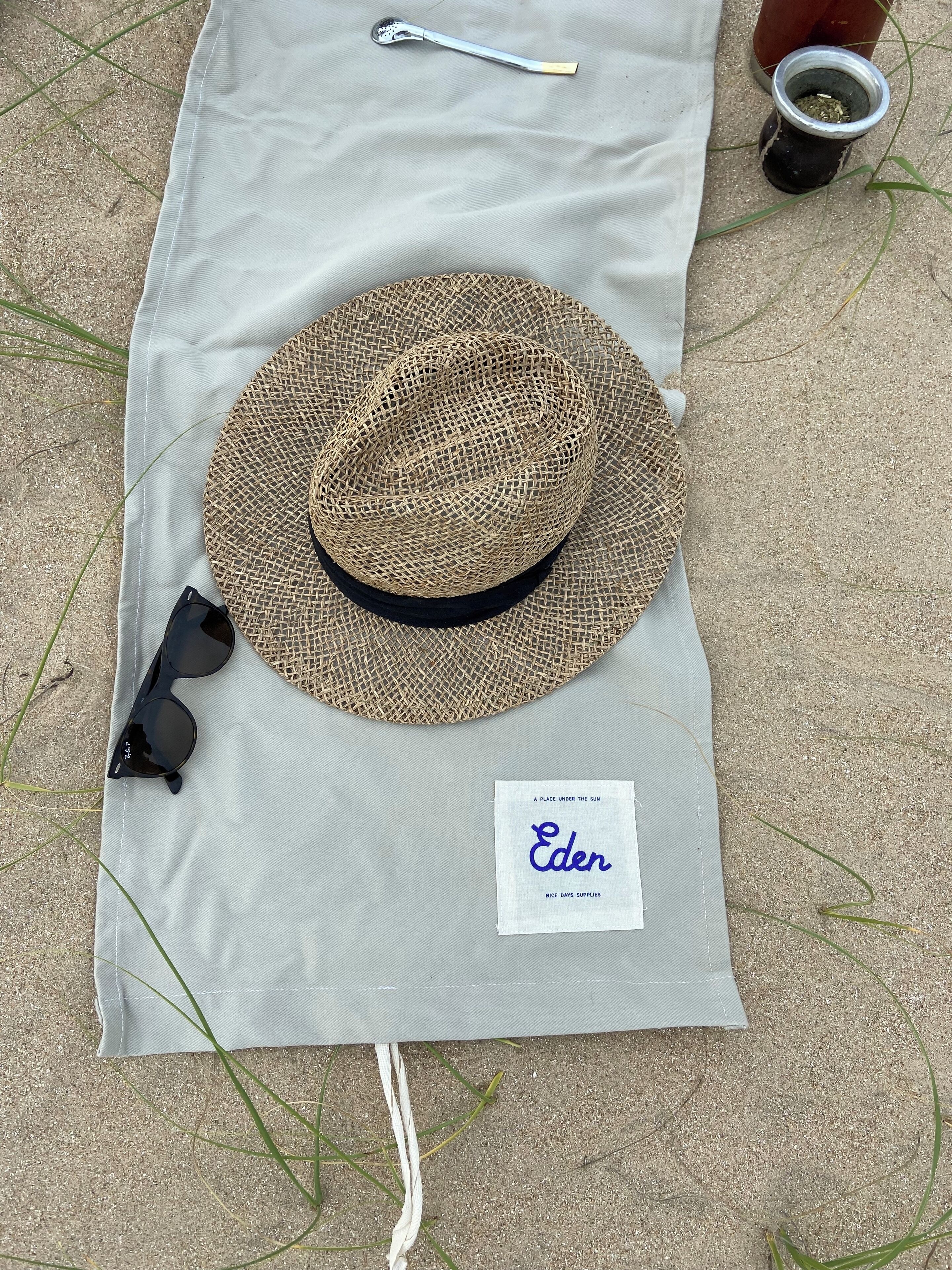 A straw hat, sunglasses, and a small sign on a beach towel.