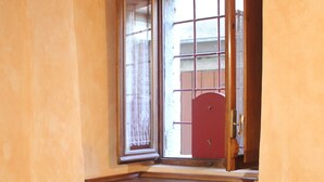 Une pièce avec un meuble en bois, une chaise blanche et une fenêtre donnant sur un bâtiment rouge à l’extérieur.