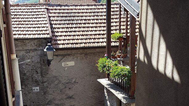 Une cour bordée de murs en pierre, surmontée d’un toit en tuiles et agrémentée de plantes en pot.