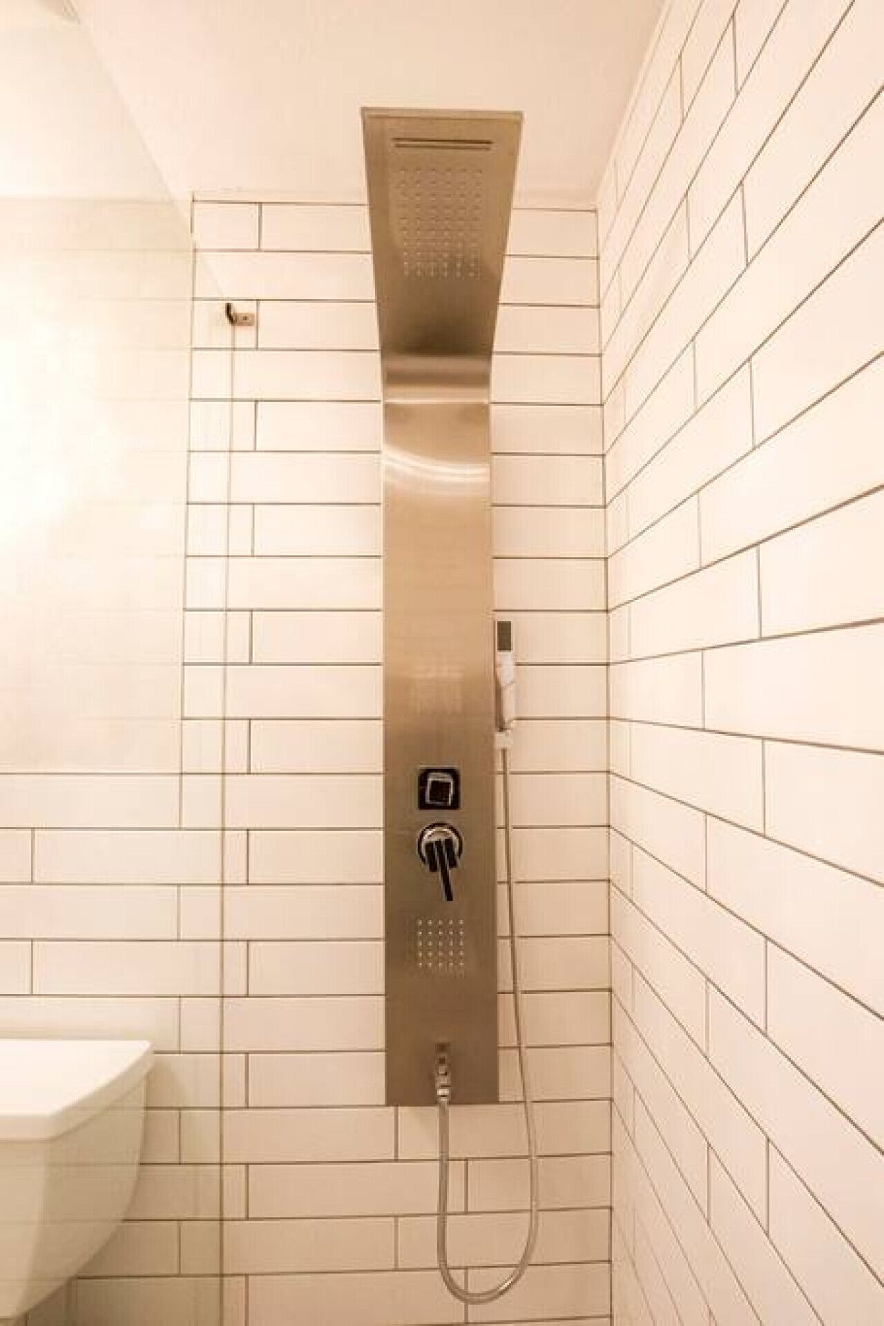 Ein modernes Badezimmer mit bodengänzender Dusche, weißen Fliesenwänden und einem weißen Waschbecken.