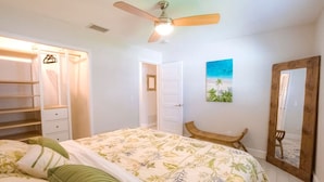 Une chambre à coucher comprenant un lit, un ventilateur de plafond, une armoire, un banc, un tableau et un miroir.