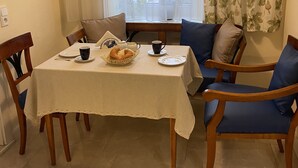 Un coin repas avec une table dressée pour deux personnes, des chaises, une fenêtre avec des rideaux et un luminaire au plafond.