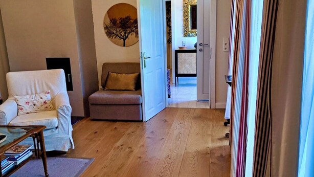 Un salon avec un canapé, une table basse et un plancher en bois. Une porte donne accès à une autre pièce.