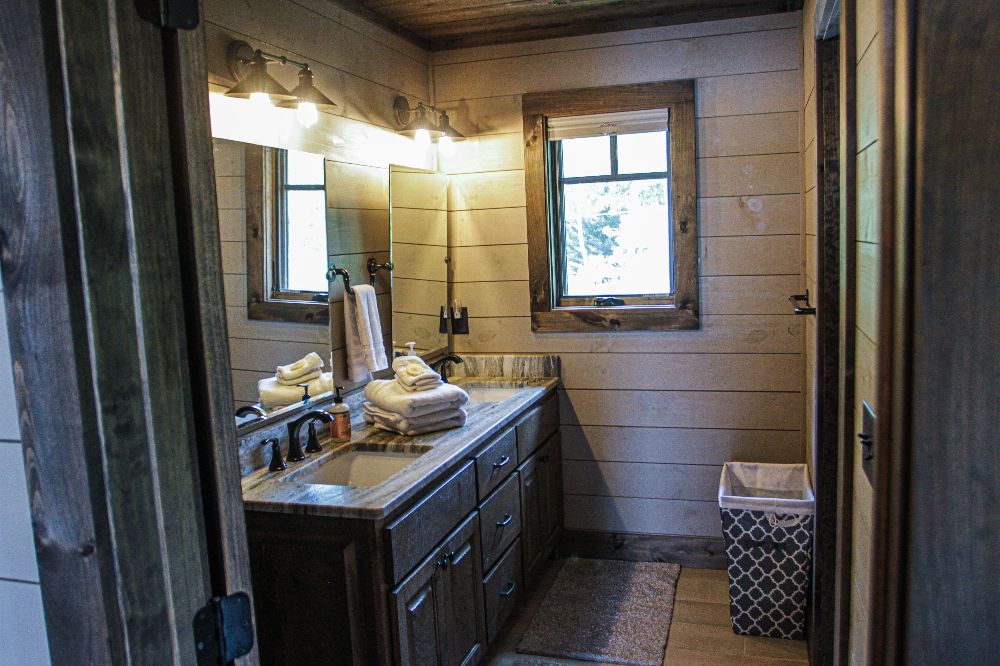 A wooden-paneled bathroom with a sink, mirror, and window.