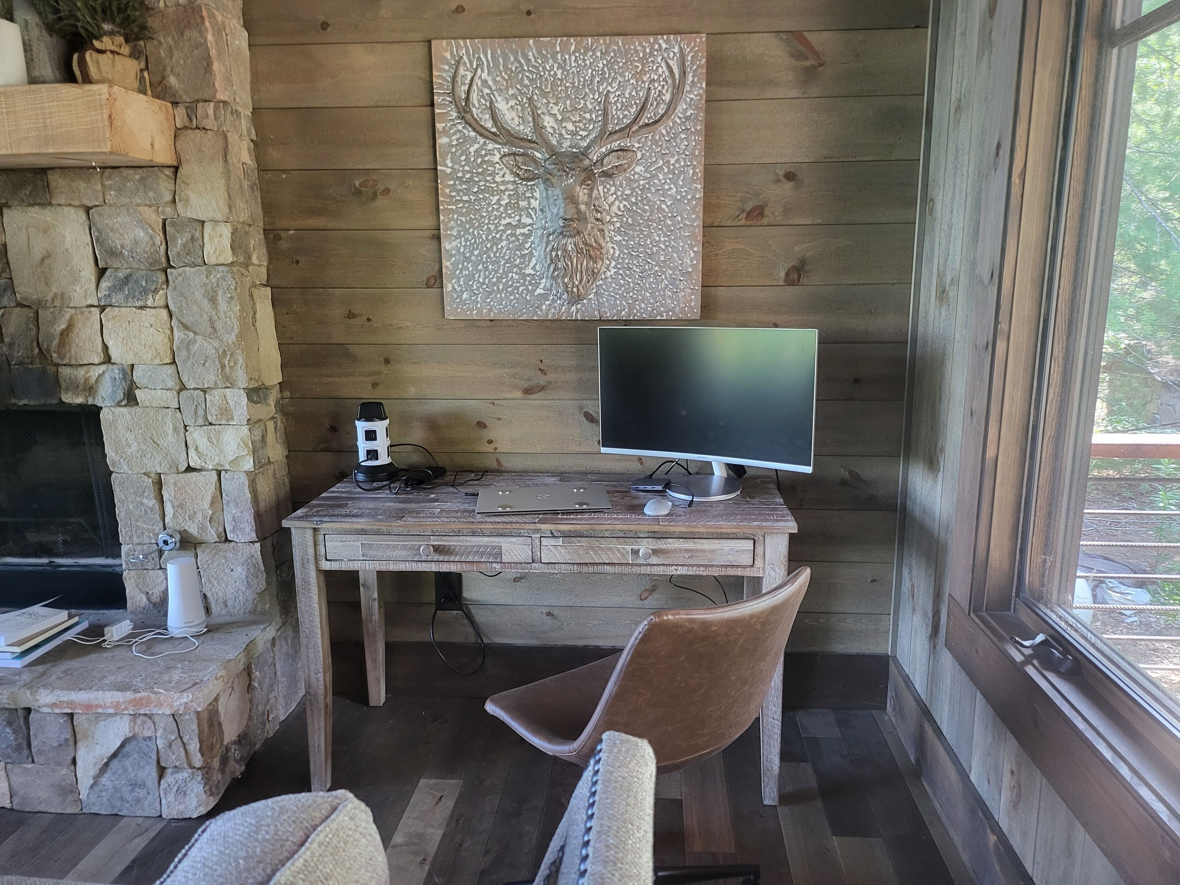A rustic room with a stone fireplace, a wooden desk with a computer, and a chair.