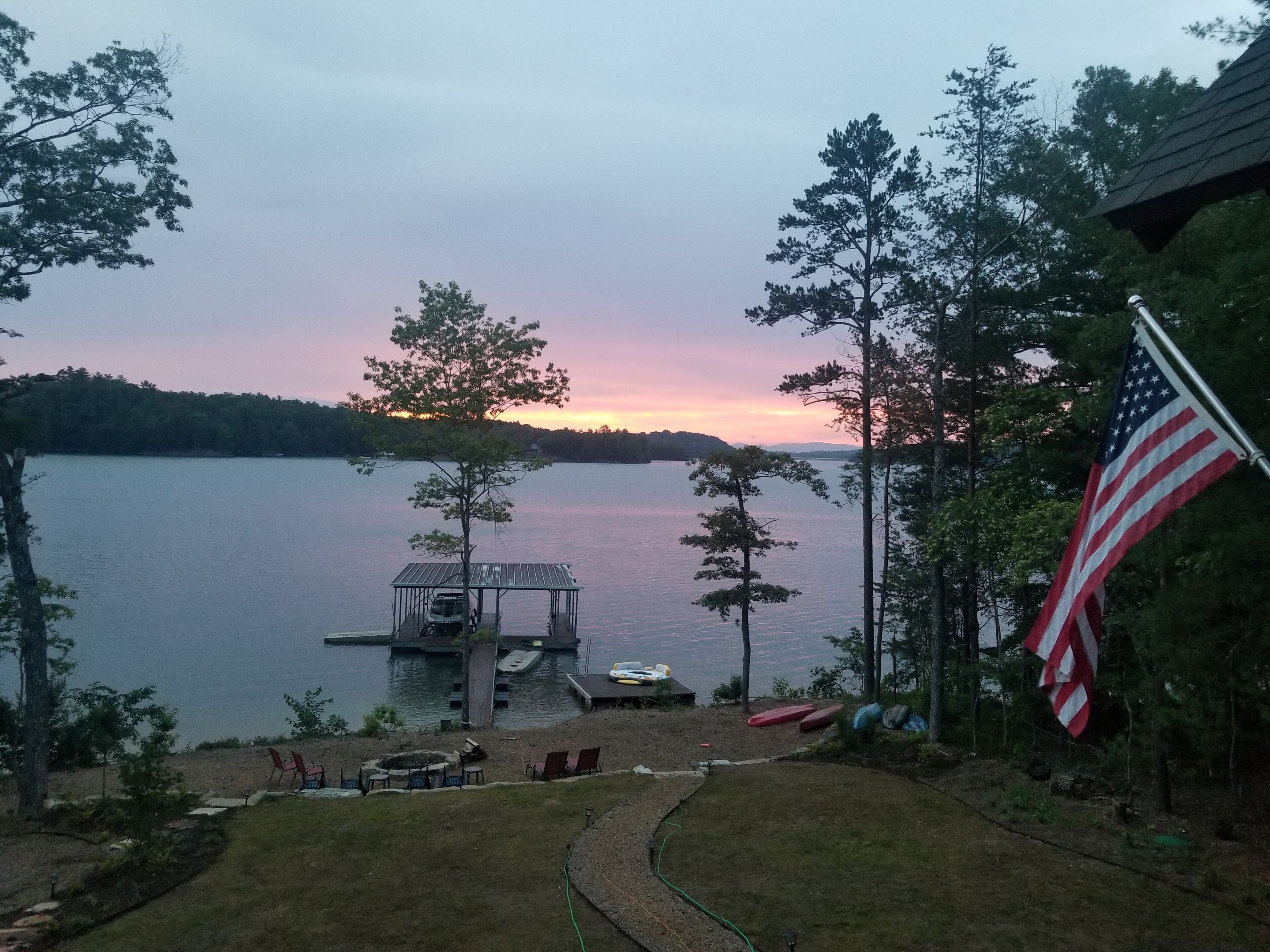 A lakeside view with a dock, chairs, and an American flag.