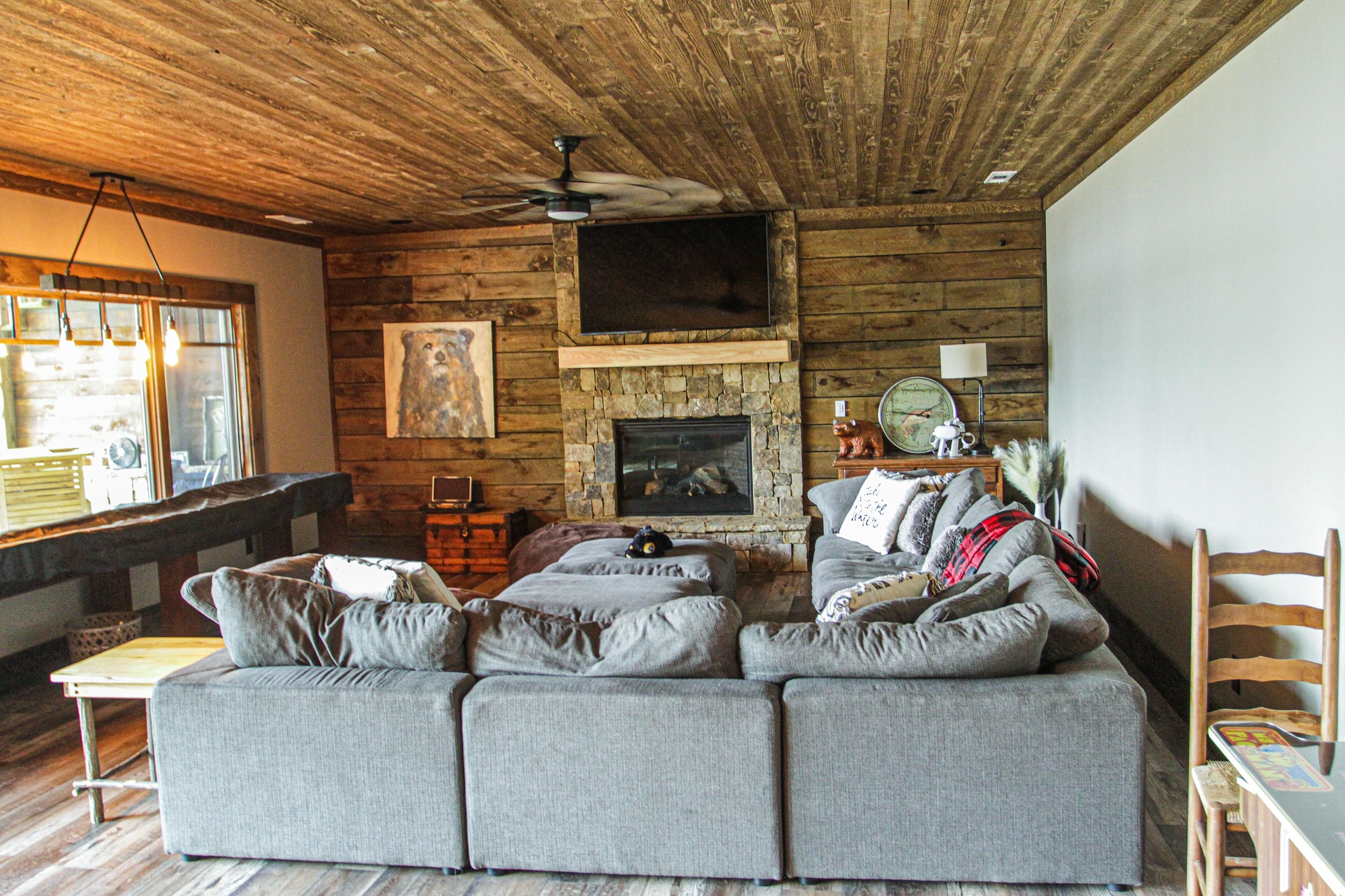 A cozy living room with a stone fireplace, a large gray sectional sofa, and a ceiling fan.