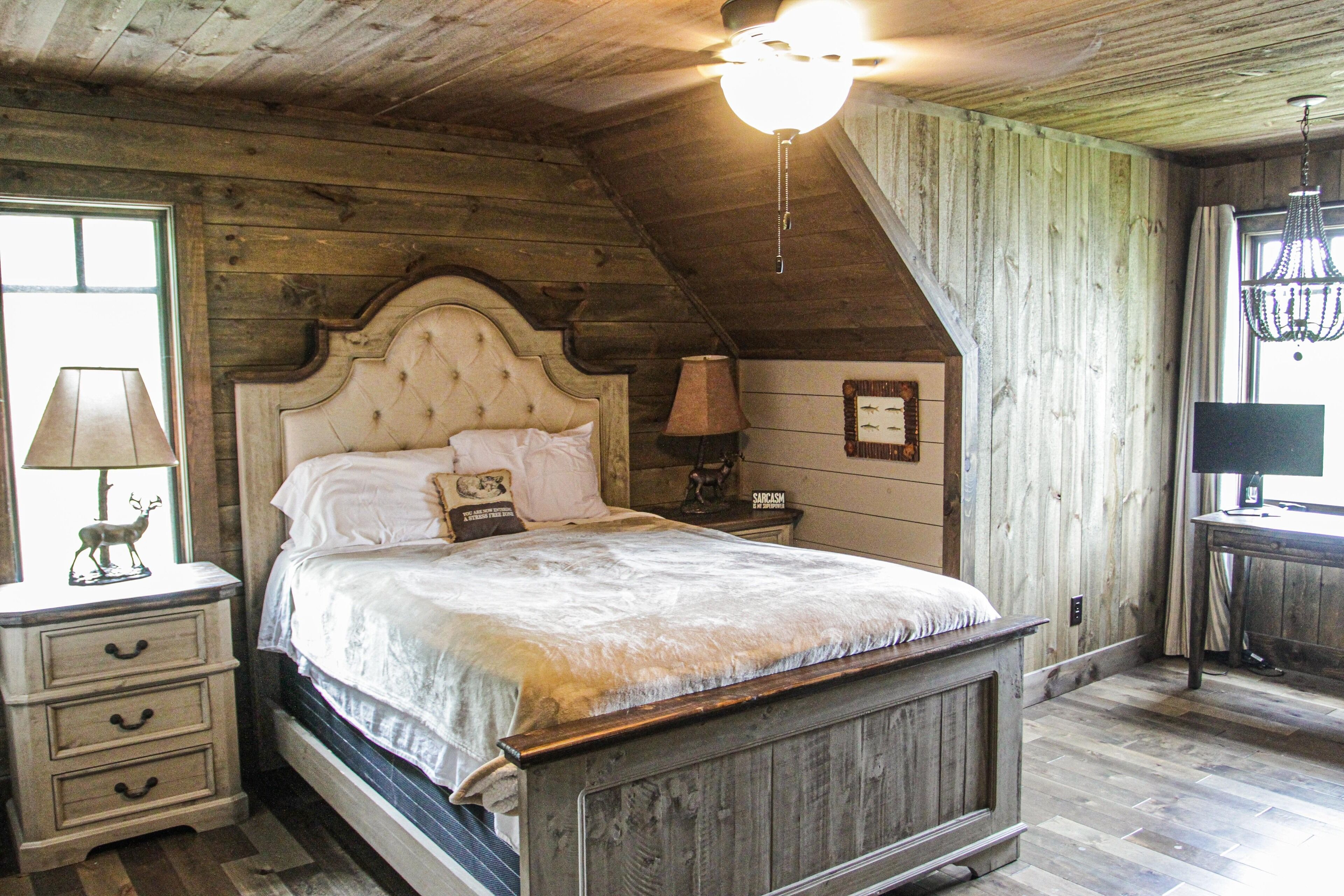 A bedroom with a wooden ceiling, a bed with a headboard, a nightstand, a lamp, and a window.