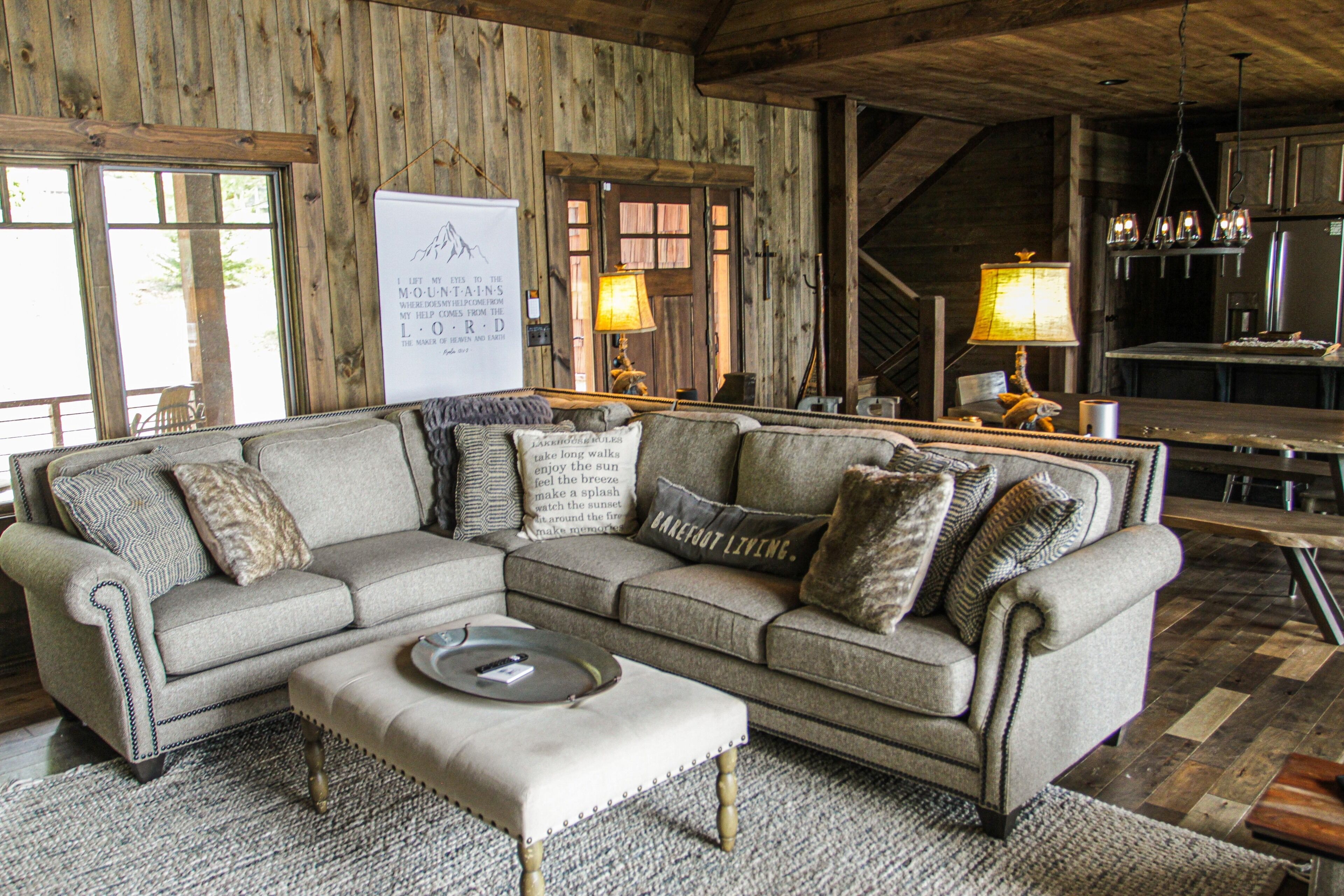 A cozy living room with a sectional sofa, ottoman, and a wooden ceiling.