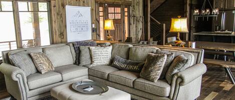 A cozy living room with a sectional sofa, ottoman, and a wooden ceiling.