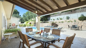 Un área de comedor al aire libre con un muro de piedra, sillas de madera y una mesa preparada para una comida.