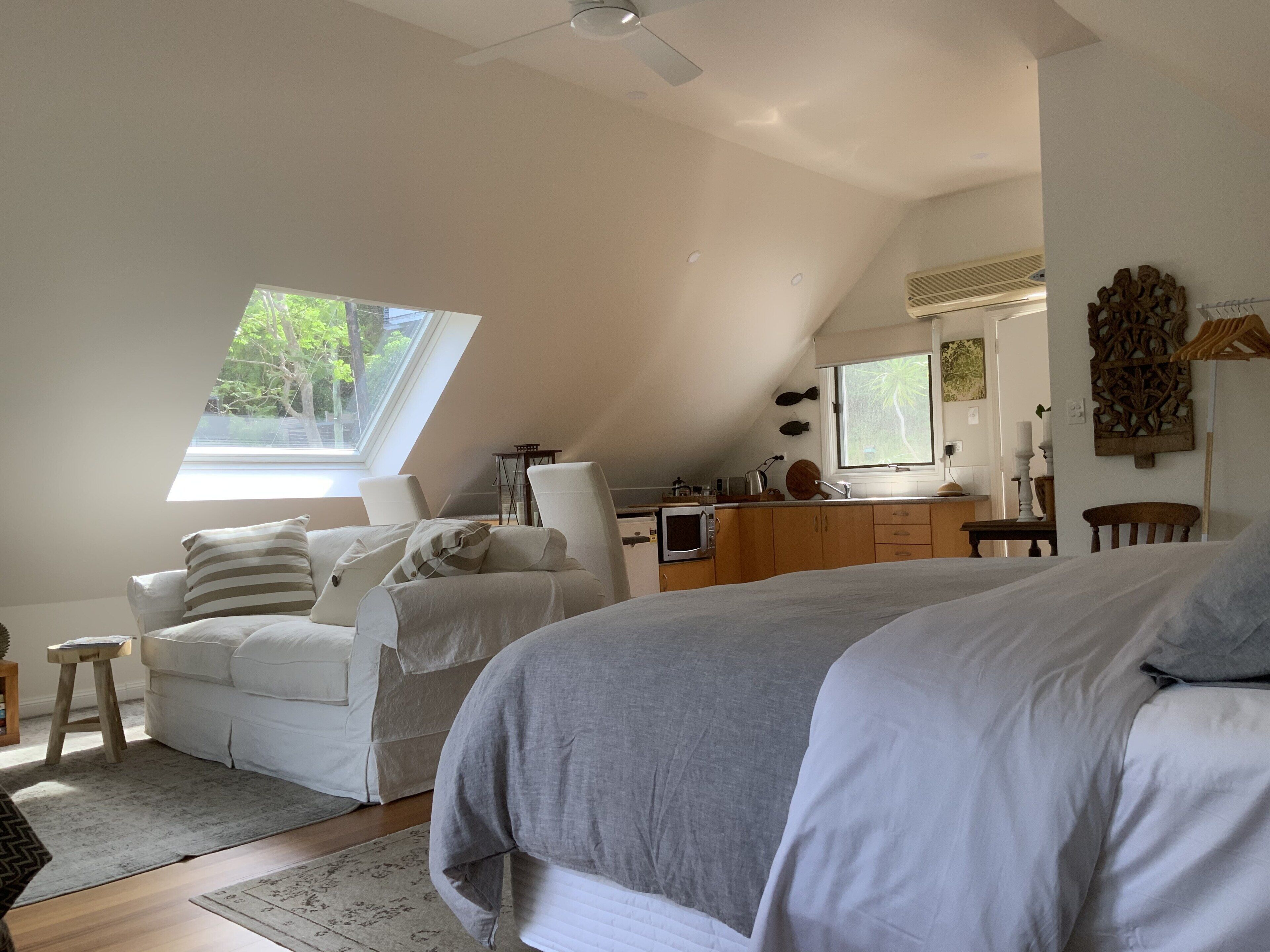 A bedroom with a large bed, a sitting area with a chair and a small table, a kitchenette, and a skylight.