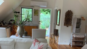 Un salon moderne avec un canapé blanc, un fauteuil en osier et un coin repas, la cuisine étant visible au fond.