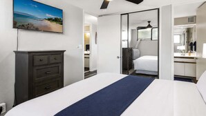 Habitación de hotel con una cama, tocador, ventilador de techo, televisión y baño visible a través de una puerta abierta.