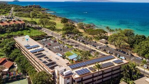 Un hotel de varios pisos, con paneles solares en el techo, estacionamiento y vista al océano.