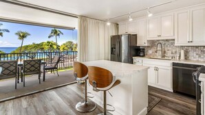 Una cocina con una isla grande, armarios blancos, electrodomésticos de acero inoxidable y vista al océano.
