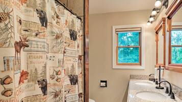 A bathroom with a shower curtain featuring nature-themed prints, a window with a view of trees, and a vanity with a mirror and sink.