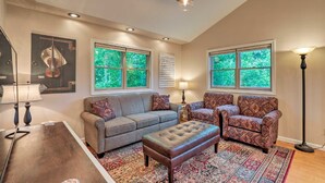 A living room with a grey sofa, patterned armchairs, a tufted ottoman, a patterned rug, and a violin painting. - Luxury lakefront apartment and private pool! Pool open Memorial Day - Labor Day. (Seneca Falls)