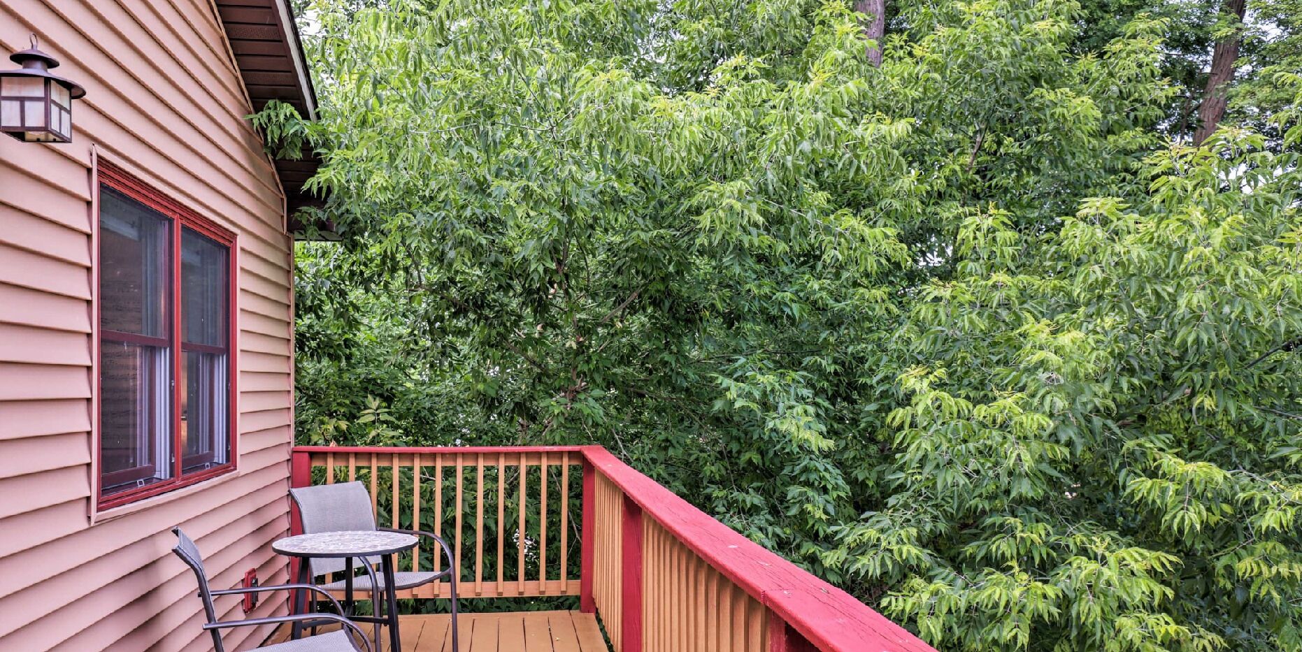 A wooden deck with a red railing, a table, and a chair.