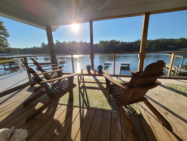 Eine Holzterrasse mit Adirondack-Stühlen und einem Tisch, mit Blick auf einen ruhigen See mit Booten und Anlegestegen.