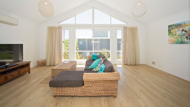 A spacious living room with a large window, a flat-screen TV, wicker furniture, and a painting on the wall. - Close to beach and town in a quiet location.  (Busselton)