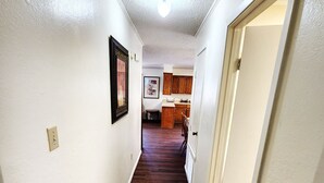 A narrow hallway with wooden flooring leading to a kitchen area.