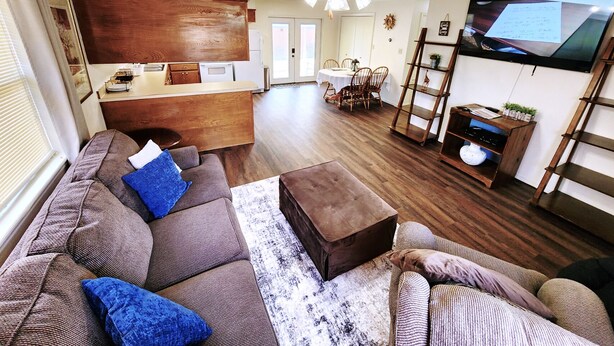 A living room with a sofa, ottoman, and a TV mounted on the wall.