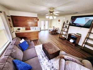 A living room with a sofa, ottoman, and a TV mounted on the wall.
