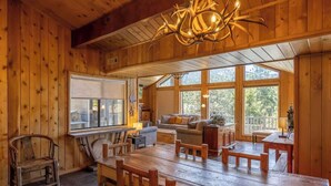 A wooden interior with a dining table, benches, a sofa, and a chandelier.