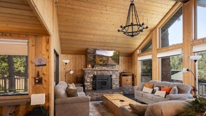 A cozy cabin interior with a stone fireplace, wooden walls, and large windows.