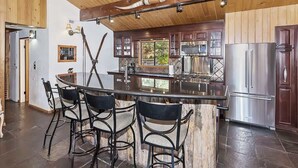 A kitchen with a central island, bar stools, stainless steel appliances, and wooden ceiling beams.