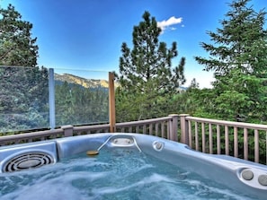 Un jacuzzi con muelle de madera y vista a una cadena montañosa boscosa.