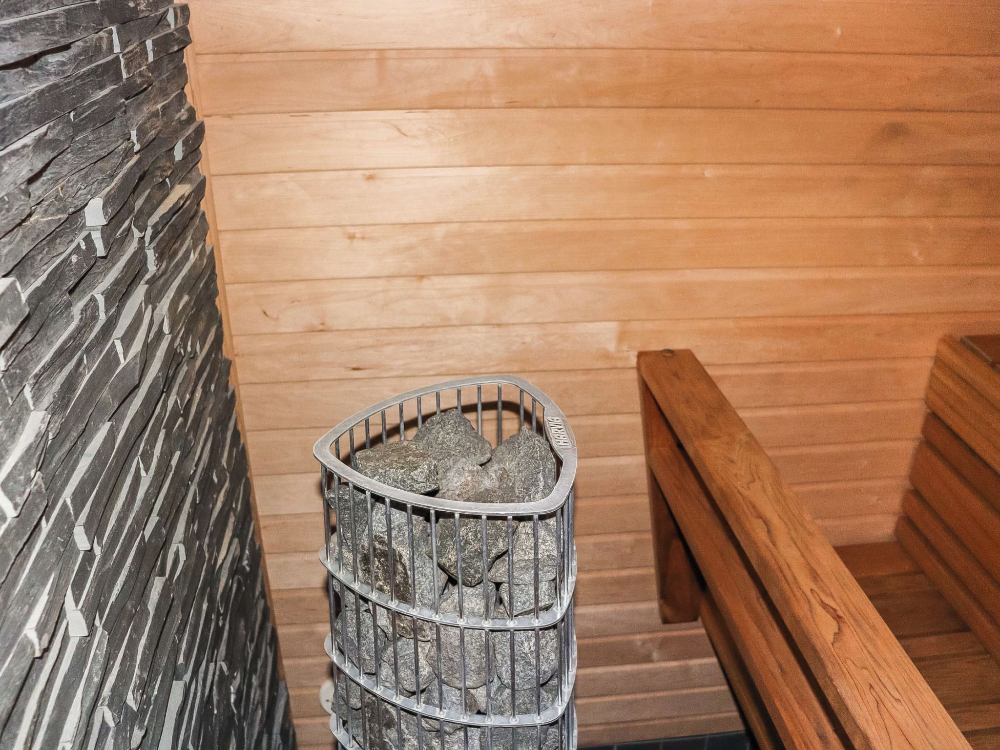A sauna with a metal container filled with stones, wooden benches, and a stone wall.