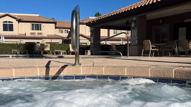 A hot tub with a metal sculpture in the foreground, surrounded by a pool area with lounge chairs and a building with a tiled roof in the background.