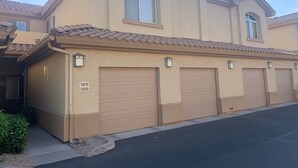 A two-story residential building with a beige facade, a tiled roof, and a garage with three doors.