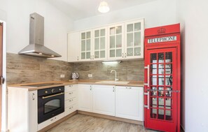 Une cuisine avec des meubles blancs, une cabine téléphonique rouge et un four moderne.