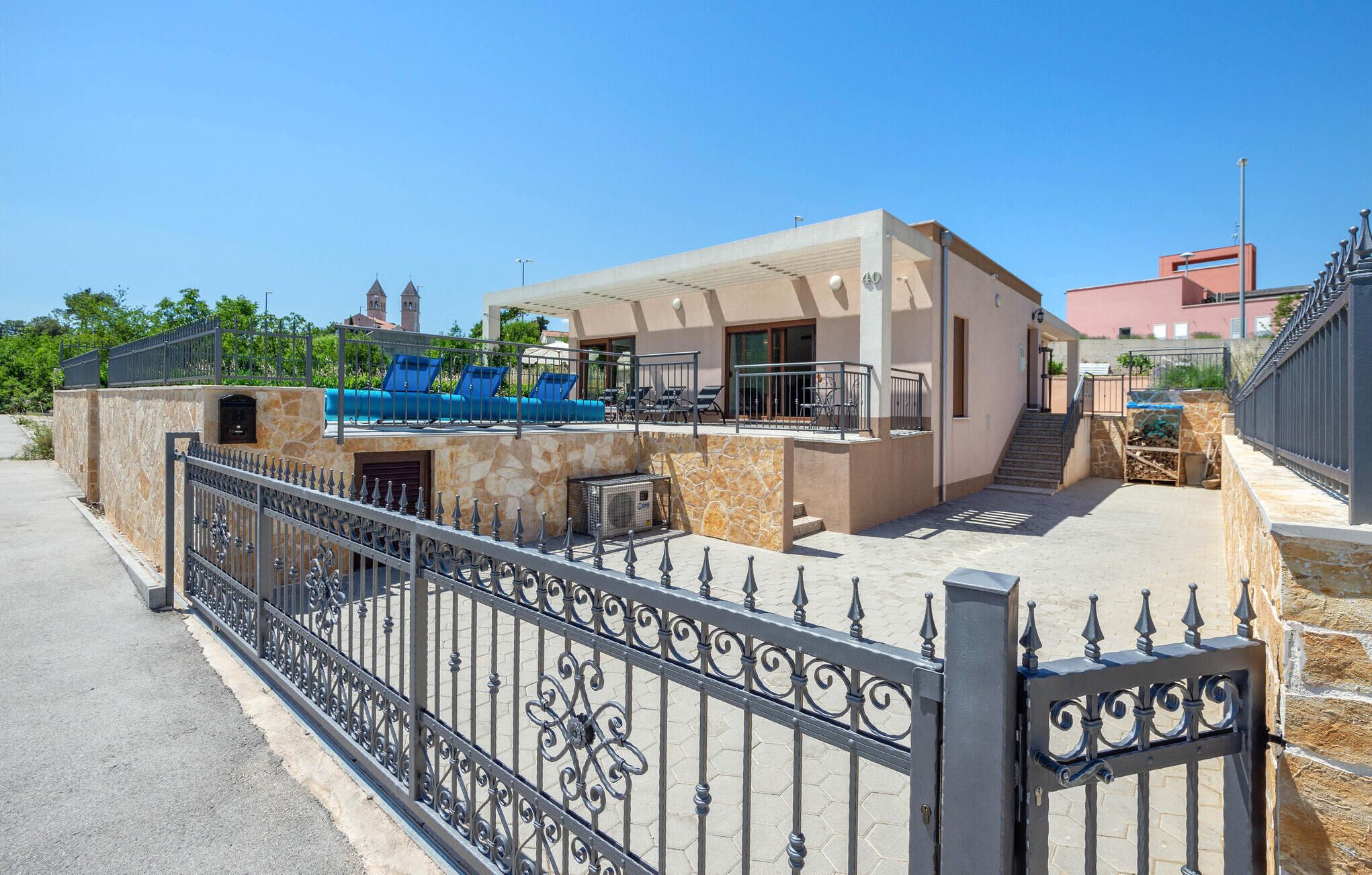 A modern two-story house with a stone facade, a balcony with blue chairs, and a gated entrance.