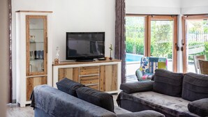 A living room with a television on a wooden cabinet, a sofa, and a view of a pool through large glass doors. - Nice home in Dugopolje with sauna (Dugopolje)