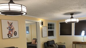 A modern living room with a brown leather sofa, a black armchair, a dining table with a lamp, and a ceiling fan. - Sunshine Villa One (Jacksonville)