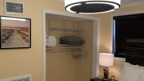 A hotel room with a bed, a nightstand with a lamp, a picture on the wall, a window with blinds, and a closet with shelves. - Sunshine Villa One (Jacksonville)