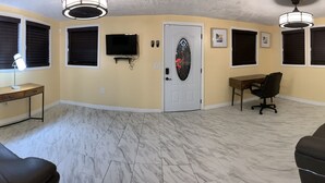 A room with a sofa, a desk, a chair, a TV, and a door. - Sunshine Villa One (Jacksonville)
