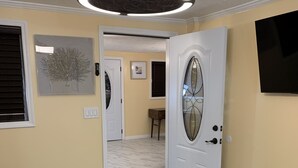 A hallway with a white door, a gray and white rug, a ceiling light fixture, and a framed picture on the wall. - Sunshine Villa One (Jacksonville)