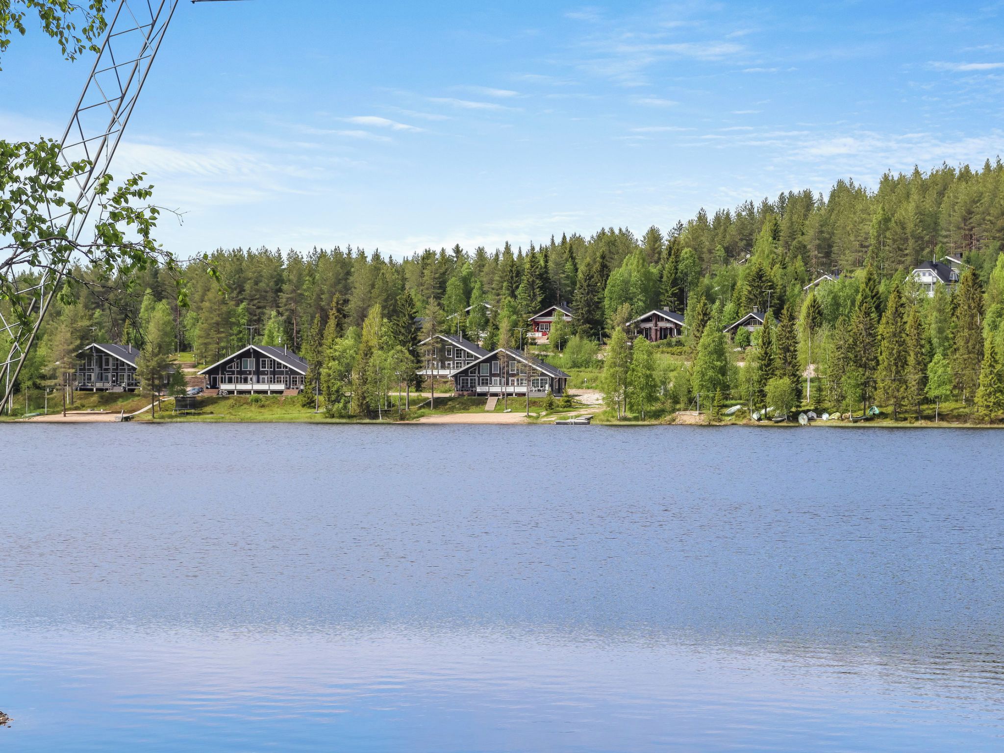 Järvenrantatontti, jossa on useita mökkejä, ja sitä ympäröi tiheä metsä sekä rauhallinen järvi.