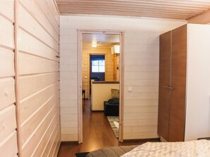 Un couloir étroit aux murs en bois mène à une pièce où se trouvent un lit et une fenêtre.
