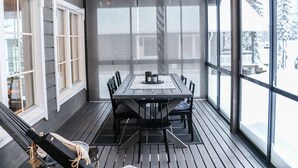 Et overdækket udendørs spiseområde med et bord, stole, store vinduer og en hængekøje.