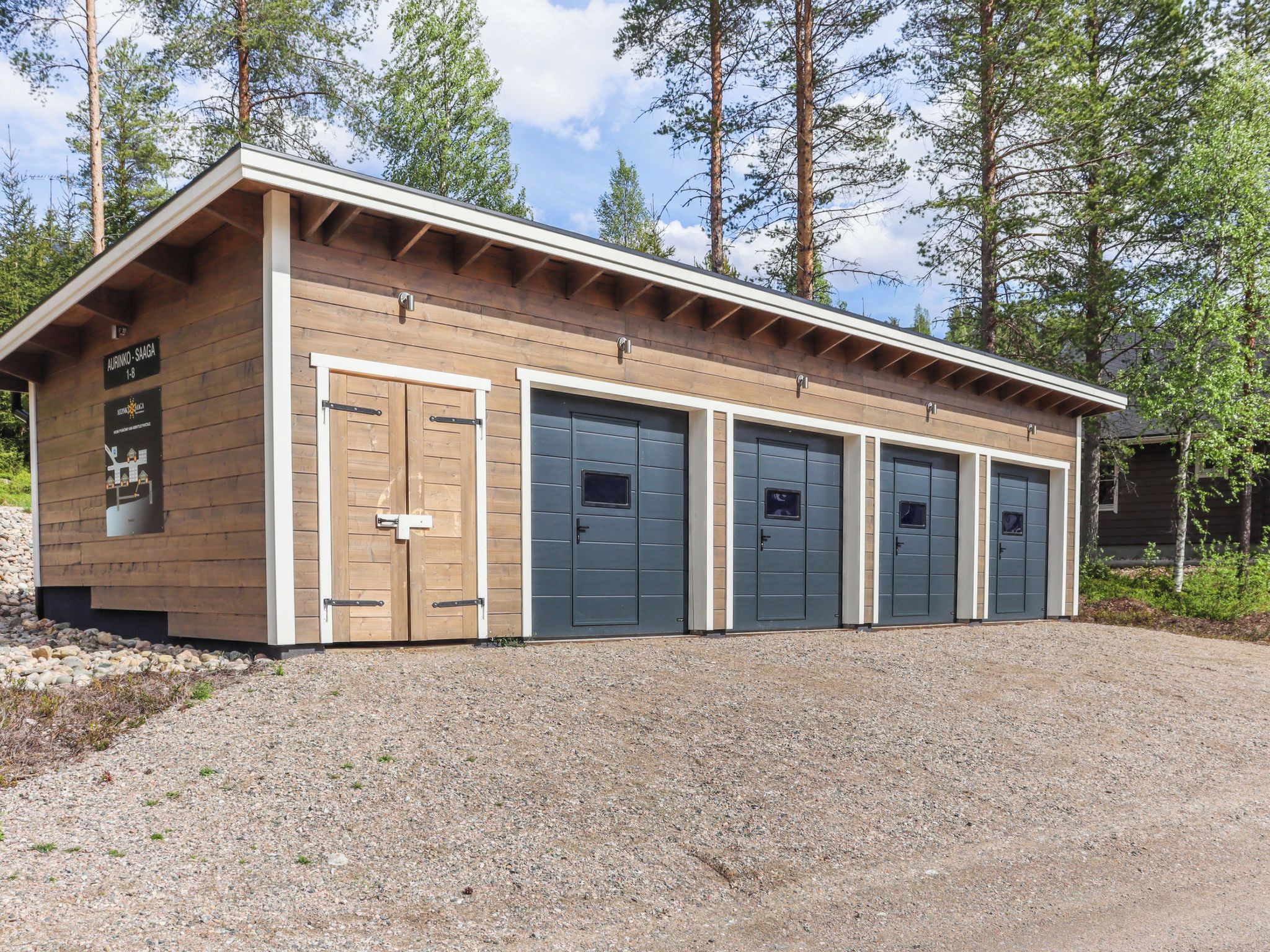 En bygning med træfacade, grusvej og et skilt der viser 'AURINNO-SAAGA I-8'.