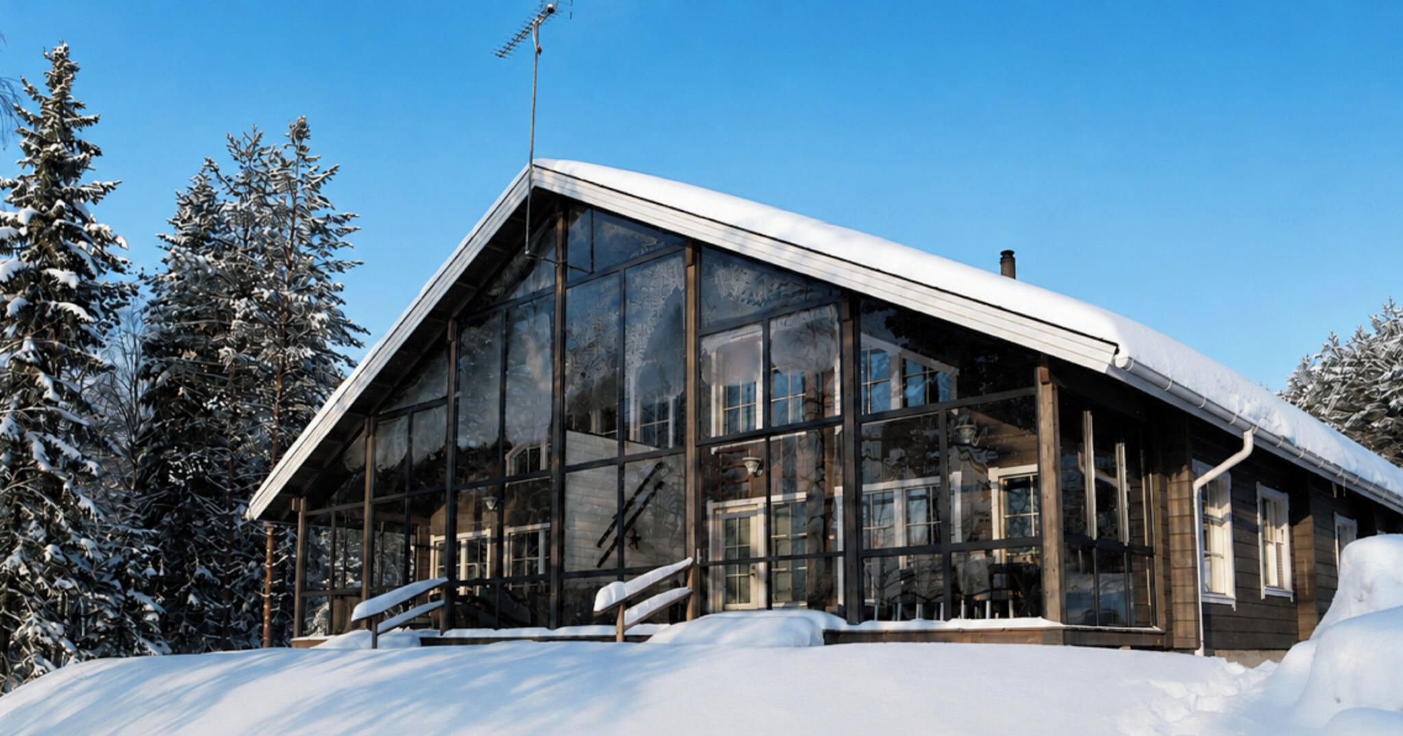 Ein modernes Gebäude mit großen Glasfenstern und einem geneigten Dach, umgeben von schneebedeckten Bäumen.