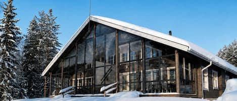 Ein modernes Gebäude mit großen Glasfenstern und einem geneigten Dach, umgeben von schneebedeckten Bäumen.