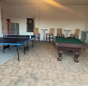 Une pièce équipée d’une table de ping-pong, d’une table de billard et de quatre chaises.