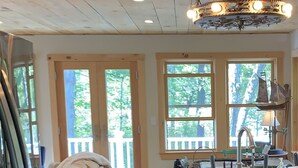 A kitchen with a dishwasher, sink, and wooden cabinets. There are large windows with a view of trees. - LAKESIDE RETREAT!  A HIDDEN GEM!!! (Ossipee)